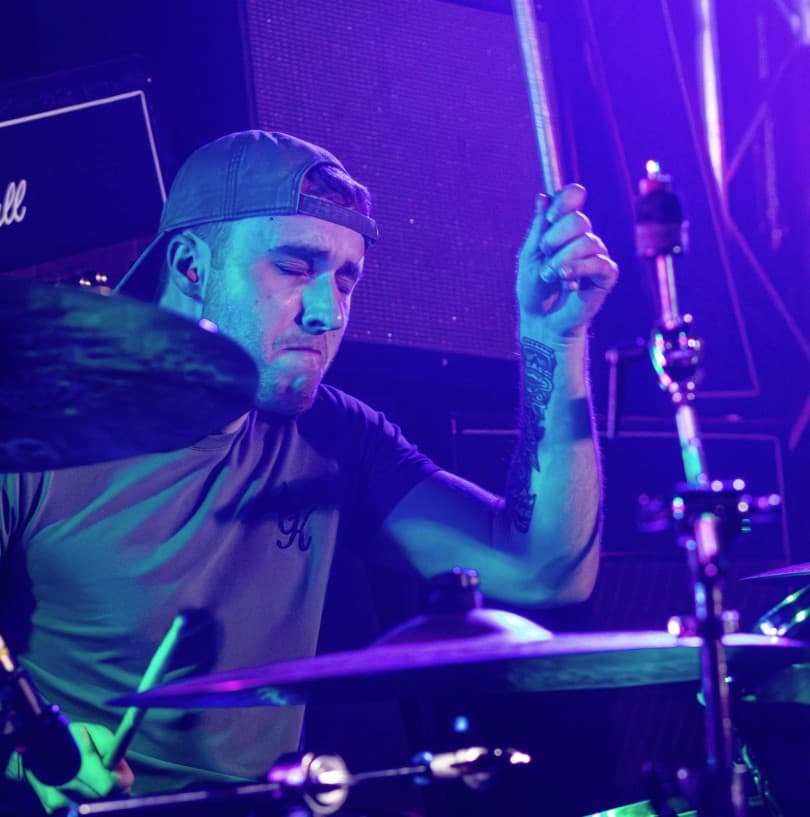 Drummer mid-strike under purple wash